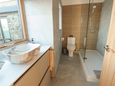 A bathroom with a marble sink basin near a window a toilet and a shower enclosure at Cuddfan in Llanfwrog near Bodedern