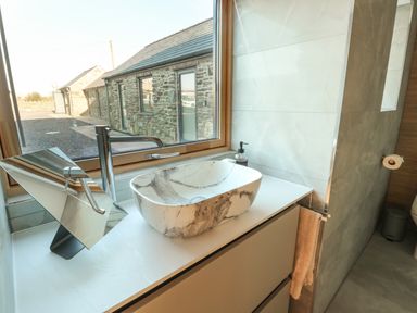 A bathroom countertop with a marble sink and a modern faucet near a window with a view of stone buildings at Cuddfan in Llanfwrog near Bodedern