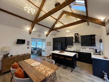 A kitchen and dining area with wooden beams and black cabinets at Cuddfan in Llanfwrog near Bodedern