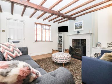 A living room with wooden ceiling beams fireplace patterned ottoman and two sofas at Chestnut Cottage in Wetwang near Great Driffield