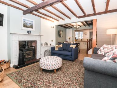A living room with a fireplace blue sofas a patterned ottoman and a dining area in the background at Chestnut Cottage in Wetwang near Great Driffield