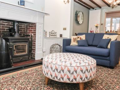 A living room with a blue sofa decorated with cushions a round patterned ottoman and a fireplace at Chestnut Cottage in Wetwang near Great Driffield