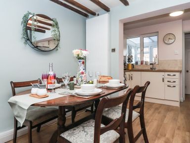 A dining area with a set table and wooden chairs next to a kitchen with cabinets and a sink at Chestnut Cottage in Wetwang near Great Driffield