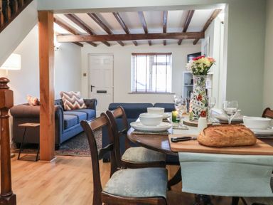 A dining area with set table and loaf of bread next to a living room with sofas and wooden beams at Chestnut Cottage in Wetwang near Great Driffield