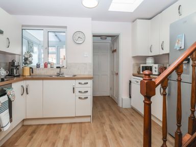 A kitchen with white cabinets wooden countertops a microwave a refrigerator a sink under a window and wooden stairs at Chestnut Cottage in Wetwang near Great Driffield