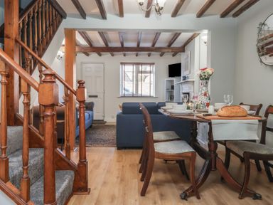 An open-plan dining and living area with wooden stairs a dining table set with dishes and bread and sofas near a window at Chestnut Cottage in Wetwang near Great Driffield
