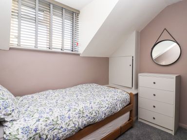 A bedroom with a single bed with floral bedding a chest of drawers and a round mirror at Chestnut Cottage in Wetwang near Great Driffield