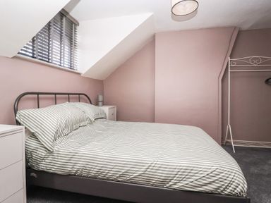 A bedroom with a striped bed, bedside tables, a window with blinds, and a metal clothing rack at Chestnut Cottage Wetwang near Great Driffield