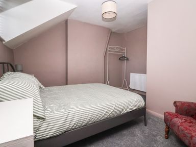 A bedroom with a bed striped bedding a red upholstered chair and a white clothes rack at Chestnut Cottage in Wetwang near Great Driffield