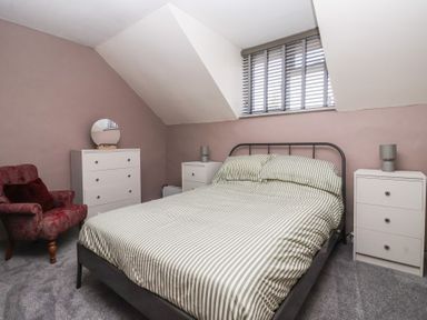 A bedroom with a double bed between two nightstands and a chest of drawers with a round mirror next to an armchair at Chestnut Cottage in Wetwang near Great Driffield