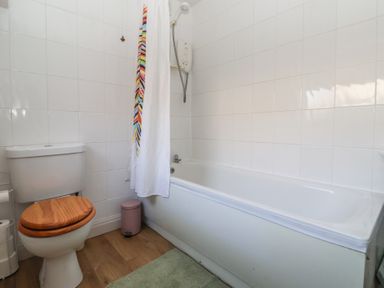 A bathroom with a toilet with wooden seat a bathtub with shower and a colorful shower curtain at Chestnut Cottage in Wetwang near Great Driffield