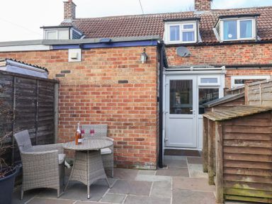 A small patio area with a table and two chairs beside a brick house at Chestnut Cottage in Wetwang near Great Driffield