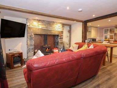 A living room with a red sofa facing a stone fireplace with a wood-burning stove and a wall-mounted TV at Miners Rest in Blaenau Ffestiniog