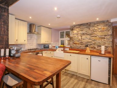 A kitchen with wooden countertops cream cabinets a stone feature wall and a small fridge at Miners Rest in Blaenau Ffestiniog