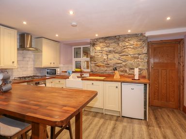 A kitchen with wooden countertops a stone wall cabinets and a wooden table at Miners Rest in Blaenau Ffestiniog
