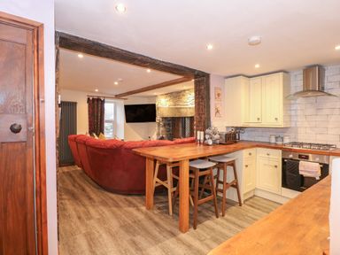 A kitchen with wooden countertops and stools next to a living room with a red sofa and stone fireplace at Miners Rest in Blaenau Ffestiniog