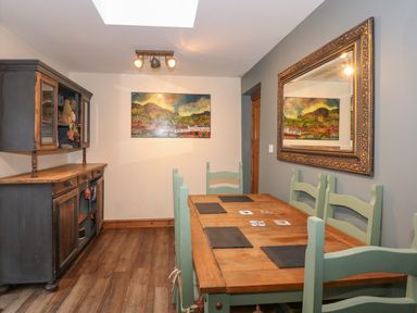 A dining room with a wooden table and green chairs a wooden cabinet and a large framed mirror at Miners Rest in Blaenau Ffestiniog