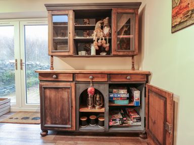 A wooden cabinet with shelves and drawers next to glass doors at Miners Rest Blaenau Ffestiniog