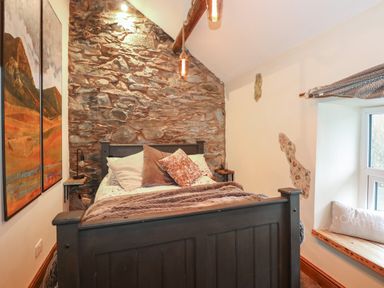 A bedroom with a stone wall behind a bed and a window seat with a cushion at Miners Rest in Blaenau Ffestiniog
