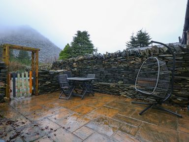 An outdoor patio with a stone wall table and chairs and a hanging chair at Miners Rest in Blaenau Ffestiniog