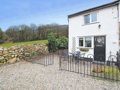 A gravel courtyard with black metal chairs and table outside a white house with a black door at Dowlais in Llanllyfni near Penygroes