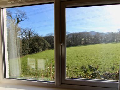A window view showing a green field with trees and a hill in the distance at Dowlais in Llanllyfni near Penygroes