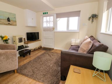 A sitting room with a brown couch, a beige armchair, a television, a small wood stove, and a wooden side table at Dowlais in Llanllyfni near Penygroes