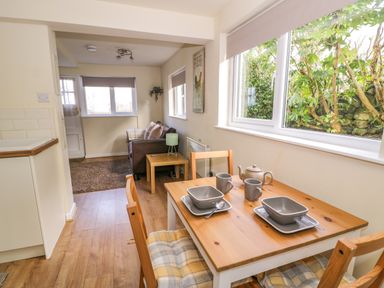 A dining area with a wooden table set for two and a small living area with a sofa and a side table with a lamp at Dowlais in Llanllyfni near Penygroes