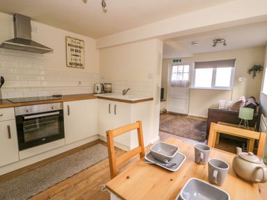 A kitchen with white cabinets and wooden countertops a table set with dishes and a teapot and a living area with a sofa and a window at Dowlais in Llanllyfni near Penygroes