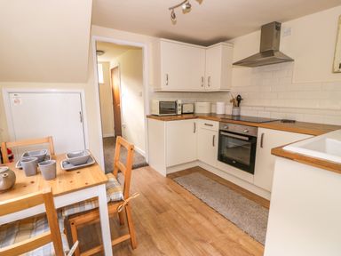 A kitchen with wooden floor a dining table with chairs plates and cups white cabinets an oven a microwave and a sink at Dowlais in Llanllyfni near Penygroes