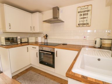 A kitchen with white cabinets wooden countertops a microwave toaster kettle and sink at Dowlais Llanllyfni near Penygroes