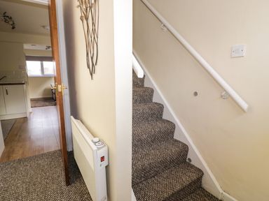 A hallway with carpeted stairs and an open door leading to a kitchen area at Dowlais in Llanllyfni near Penygroes