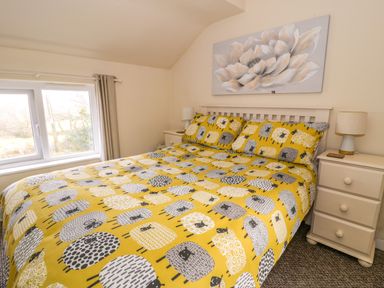 A bedroom with a bed covered in yellow sheep patterned bedding two bedside tables with lamps and a window at Dowlais in Llanllyfni near Penygroes