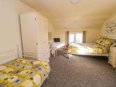 A bedroom with two beds a white wardrobe a desk with a stool a small TV on the desk a window with curtains and a painting on the wall at Dowlais in Llanllyfni near Penygroes
