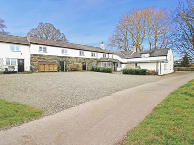 A gravel driveway in front of a long two story house with stone and white walls and leafless trees in the background at Igamogam Llanllyfni near Penygroes