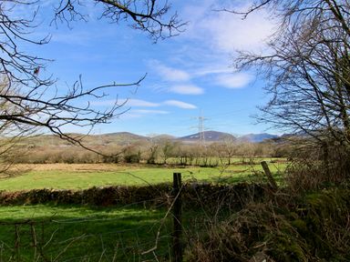 A rural field with trees power lines and hills in the background at Igamogam Llanllyfni near Penygroes