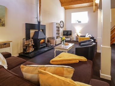 A living room with a wood-burning stove sofa chairs coffee table and television at Igamogam in Llanllyfni near Penygroes