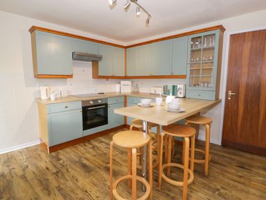 A kitchen with green cabinets wooden stools a wooden floor and a breakfast bar at Igamogam in Llanllyfni near Penygroes