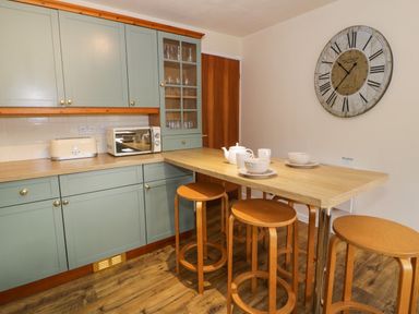 A kitchen with light green cabinets a microwave toaster wooden stools and a wall clock at Igamogam in Llanllyfni near Penygroes