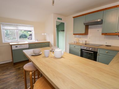 A kitchen with green cabinets wooden countertops an oven and a breakfast bar with dishes and teapot at Igamogam in Llanllyfni near Penygroes