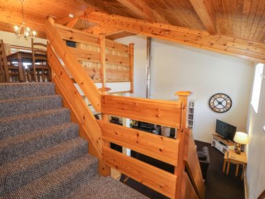 A carpeted staircase with wooden railings leading to a dining area and a living room with a TV clock and lamp at Igamogam in Llanllyfni near Penygroes