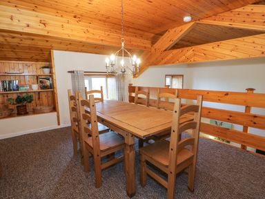 A dining area with wooden table and chairs under a wooden ceiling with built in shelves at Igamogam in Llanllyfni near Penygroes