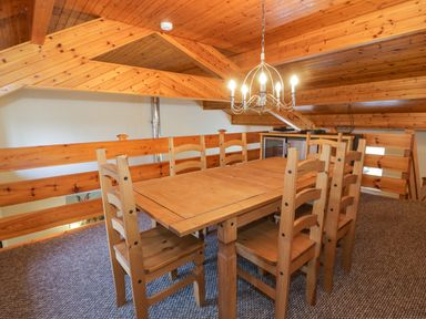 A wooden dining table with six wooden chairs under a chandelier in a room with a sloped wooden ceiling at Igamogam in Llanllyfni near Penygroes