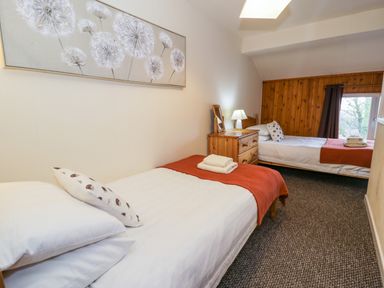 A bedroom with two single beds orange blankets a wooden nightstand and a window at Igamogam Llanllyfni near Penygroes