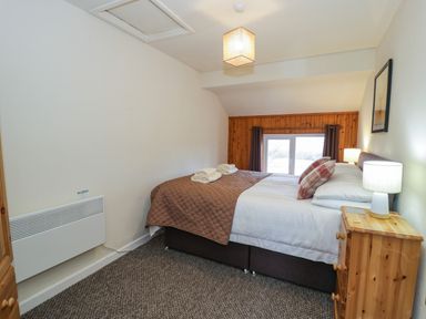 A bedroom with a double bed with pillows and lamps on wooden bedside tables at Igamogam in Llanllyfni near Penygroes