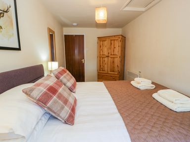 A bedroom with a bed with plaid pillows a wooden wardrobe and folded towels at Igamogam Llanllyfni near Penygroes