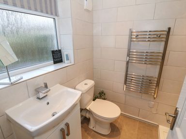 A bathroom with a sink cabinet a toilet a chrome towel radiator and a frosted window at Camwy in Brynsiencyn