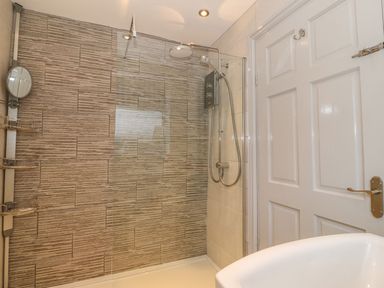A bathroom shower area with tiled walls a glass shower screen and a white door at Camwy in Brynsiencyn
