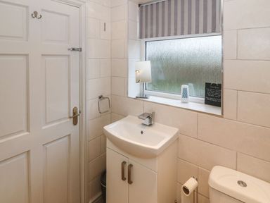 A bathroom with a white sink cabinet a frosted window and a toilet at Camwy in Brynsiencyn