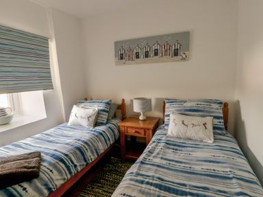 A bedroom with two single beds a wooden nightstand with a lamp between the beds and a window with striped blinds at Camwy in Brynsiencyn